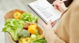 Lista de compras do mês: mulher com uma lista de compras e embaixo dentro de cestos alguns legumes.
